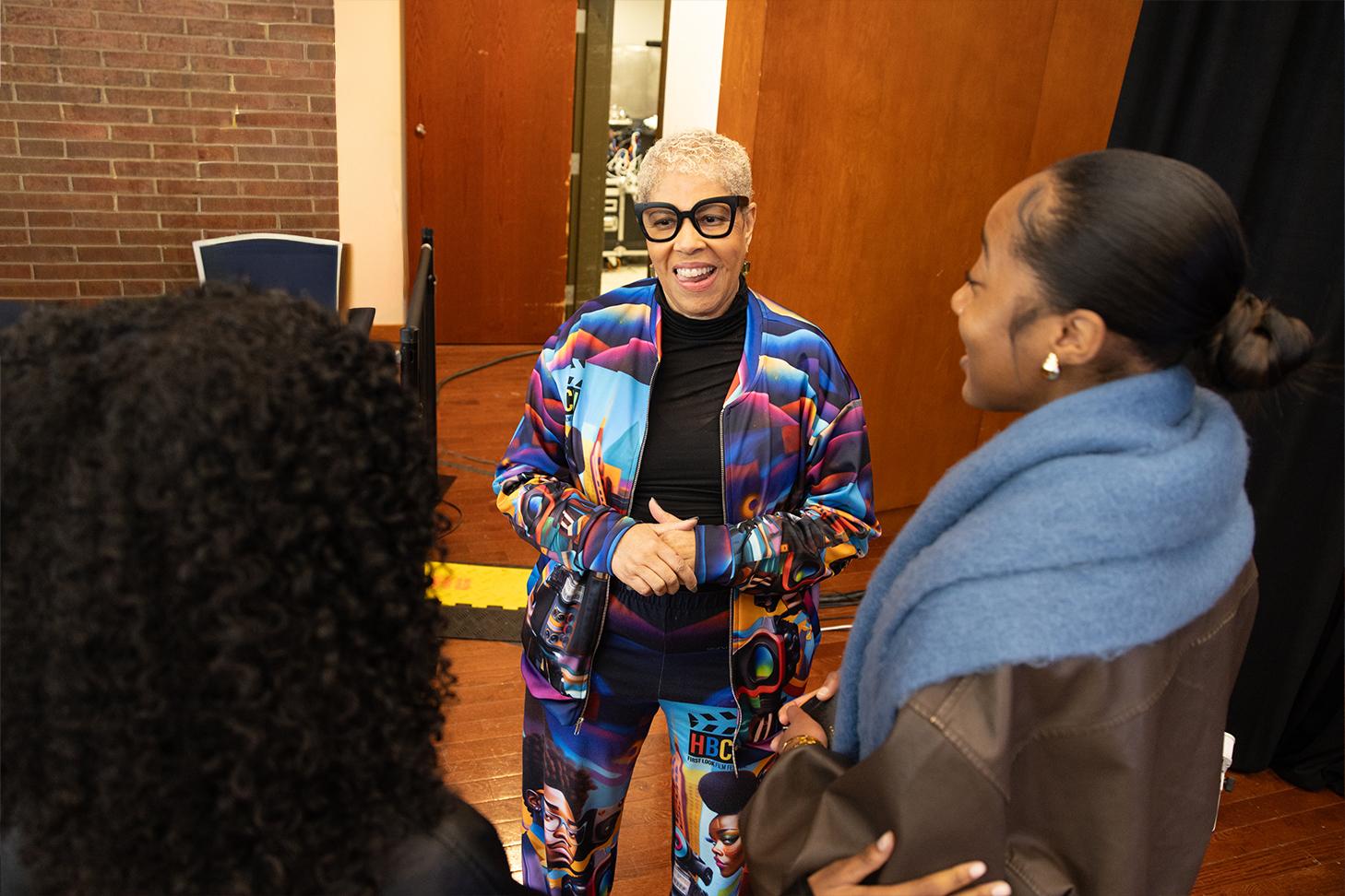 A woman standing talking to two people who have their faces turned away from the camera