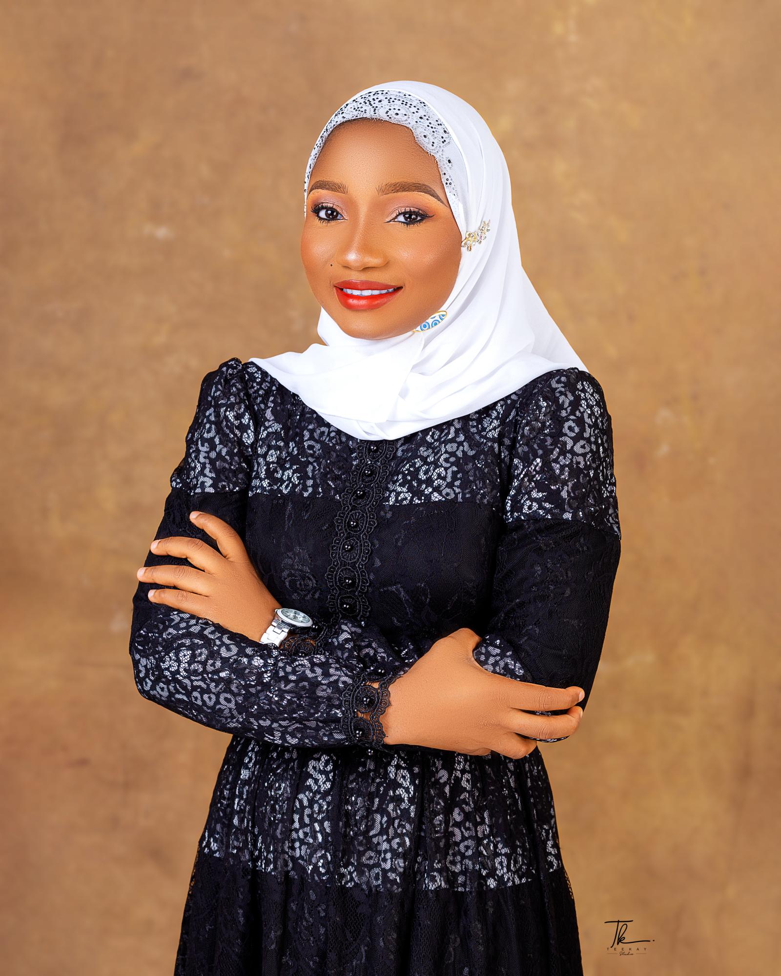 A woman wearing a white head covering is standing with her arms crossed smiling and looking at camera
