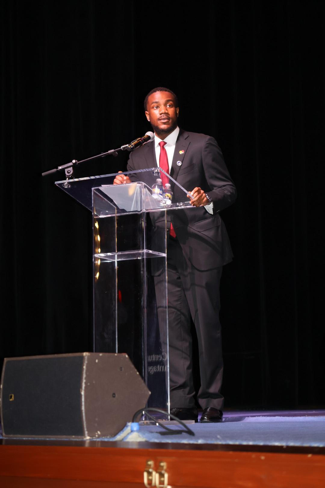 Joshua Taylor stands on stage at a glass podium