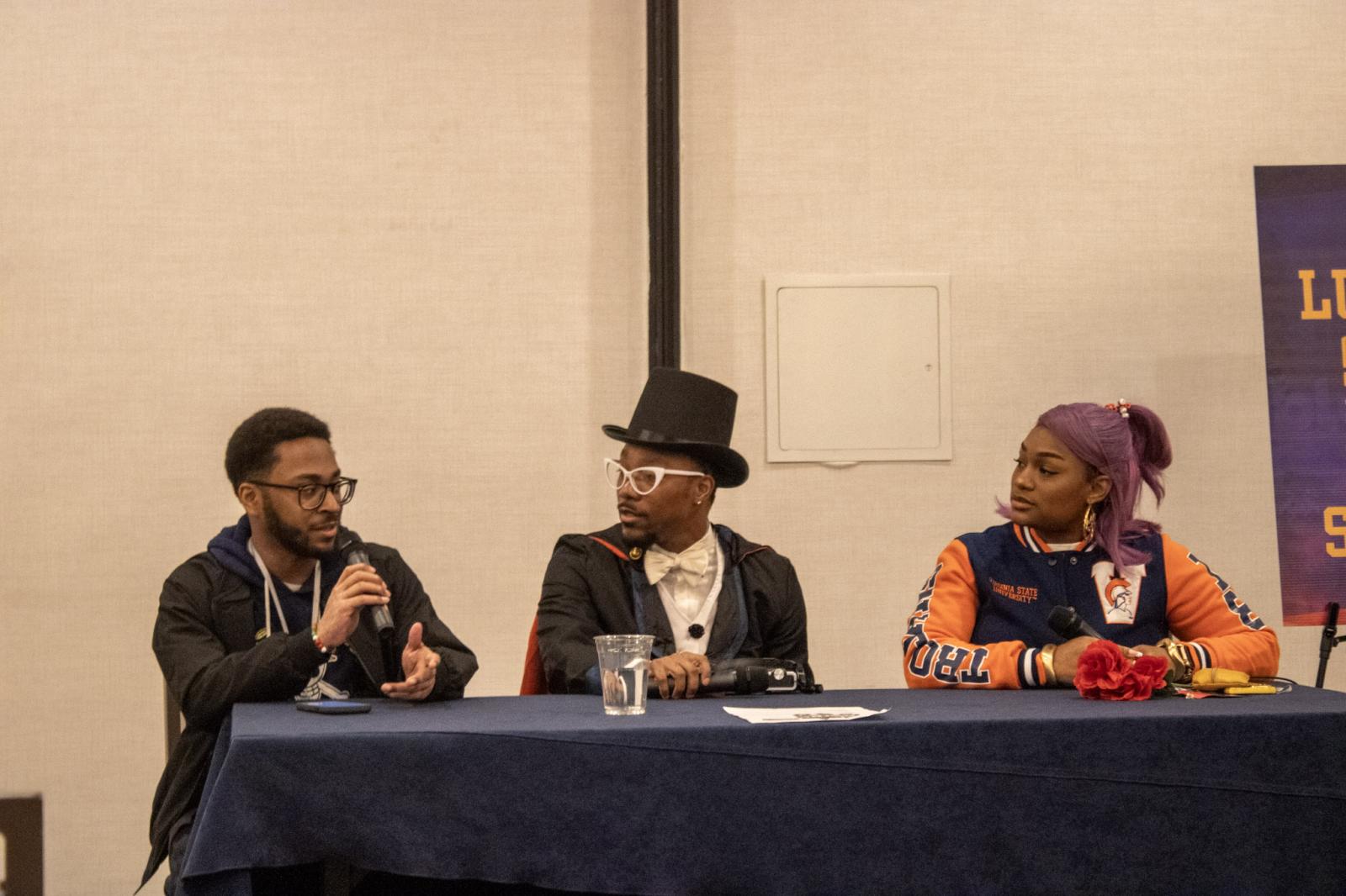 Three people sitting behind a table. the person on the far left is holding a microphone