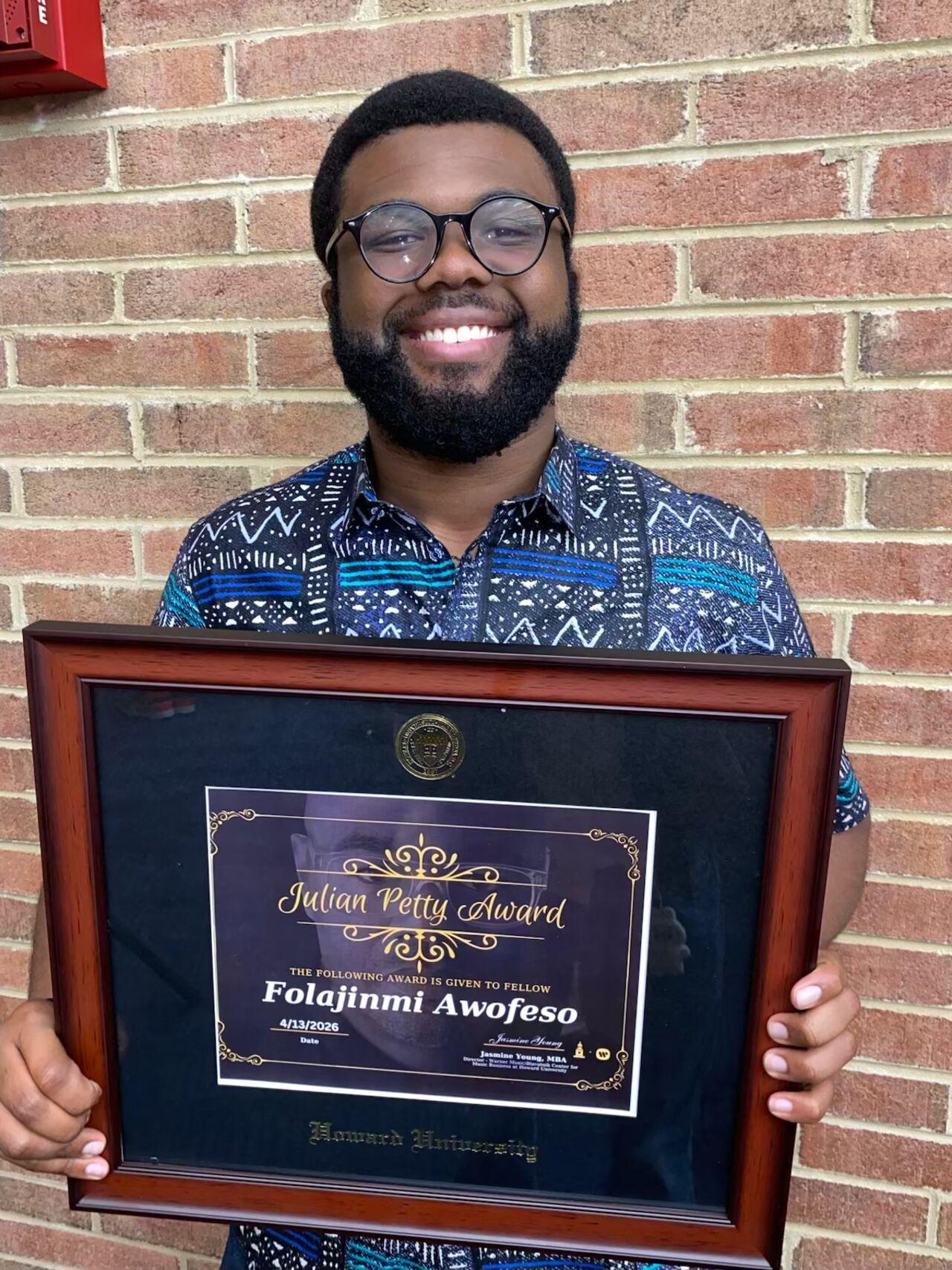 Folajinmi Awofeso holding a framed picture of a paper award