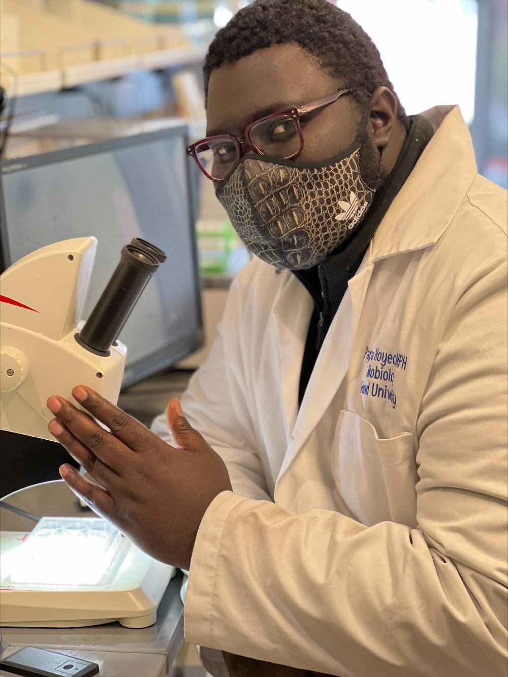 Papa Hoyeck sits at a microscope in a white lab coat