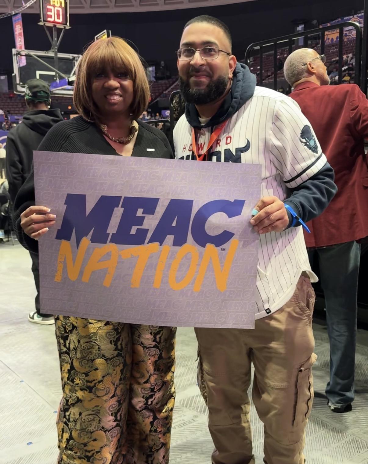 A woman and a man holding a sign that says MEAC Nation in purple and gold lettering
