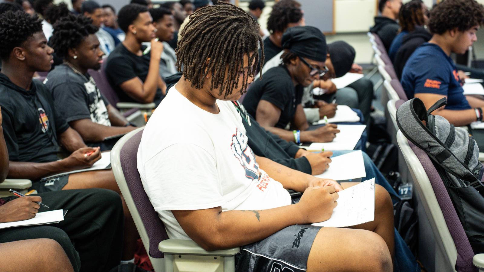 College students sitting at desks looking down at papers, writing, and looking at person out of frame