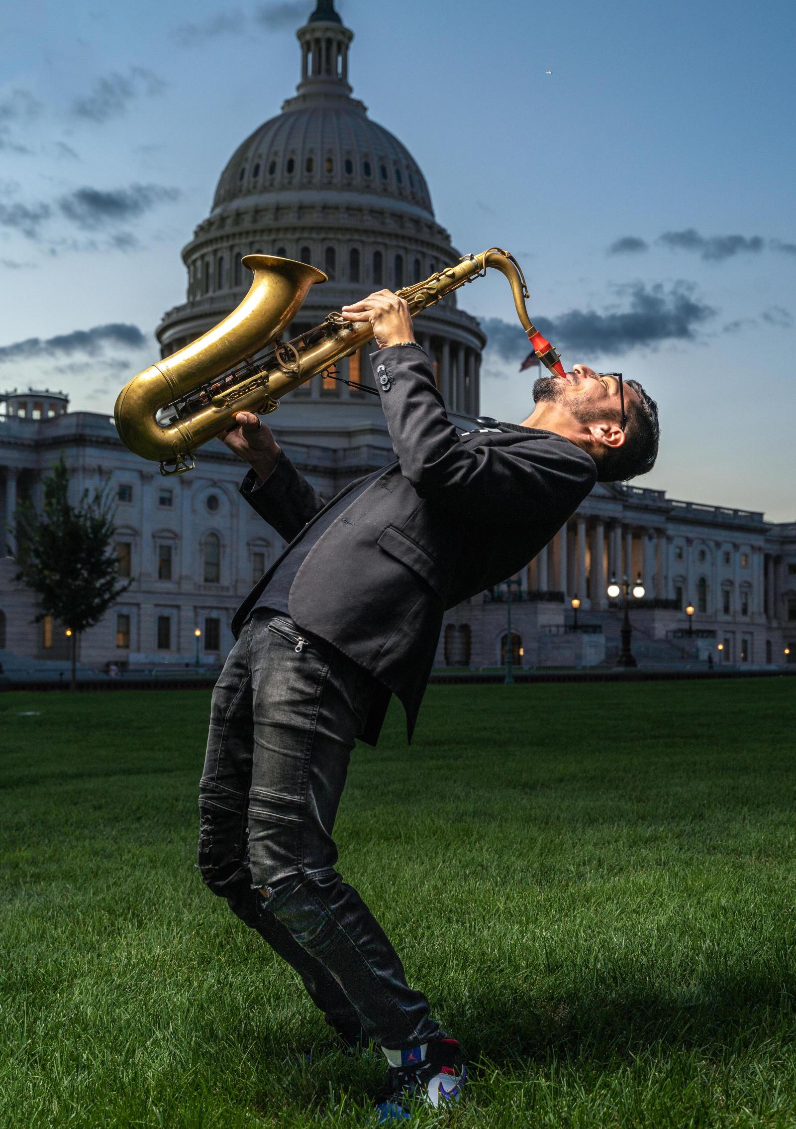 Elijah Jamal Balbed tilting and playing the saxophone upward. In the backdrop is the Capitol Building