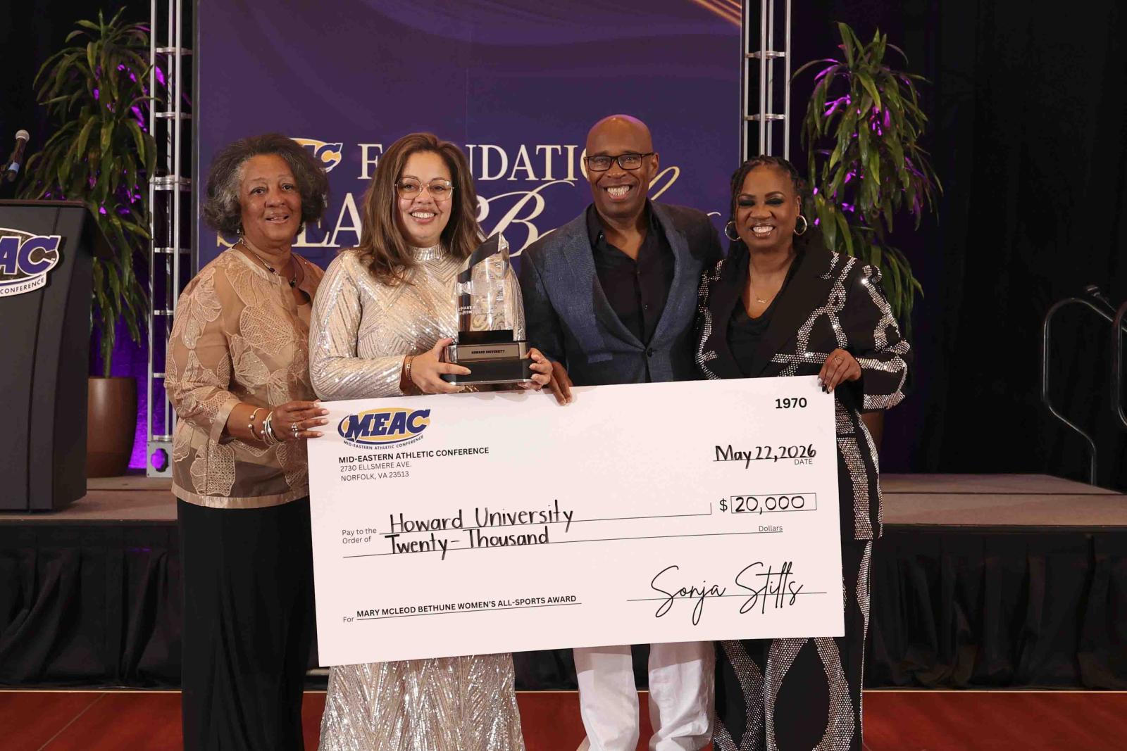 A group of four people holding a large check made out to Howard University for 20,000 dollars