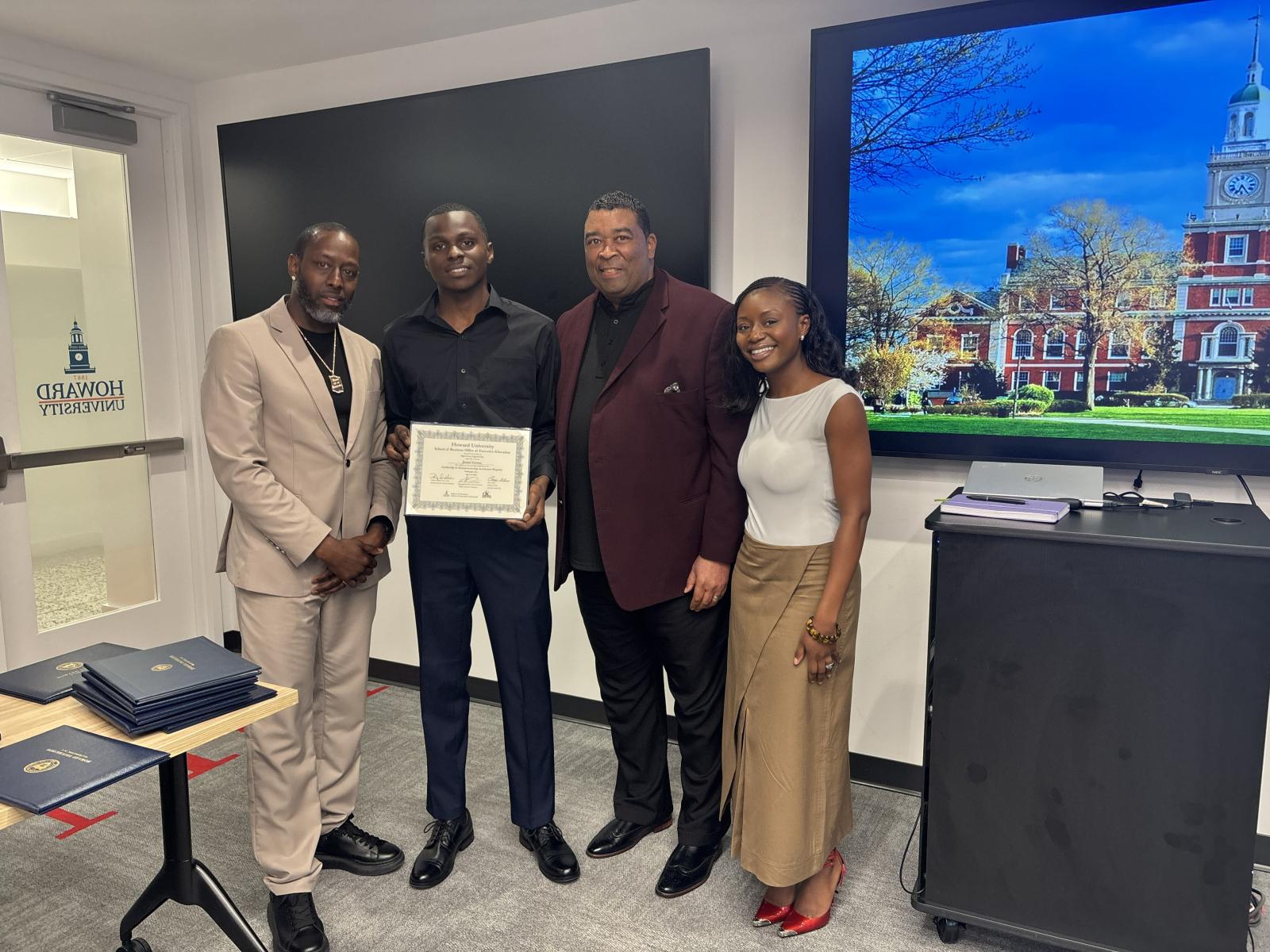 Four people standing next to each other. The second person on the left is holding a certificate