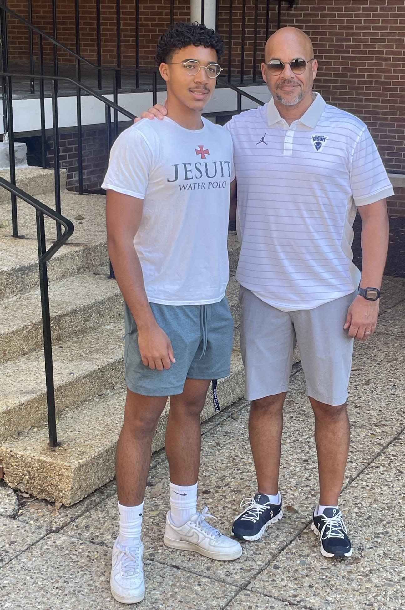 A son and father side by side smiling at the camera while outside. There is a small set of steps behind the person on the left