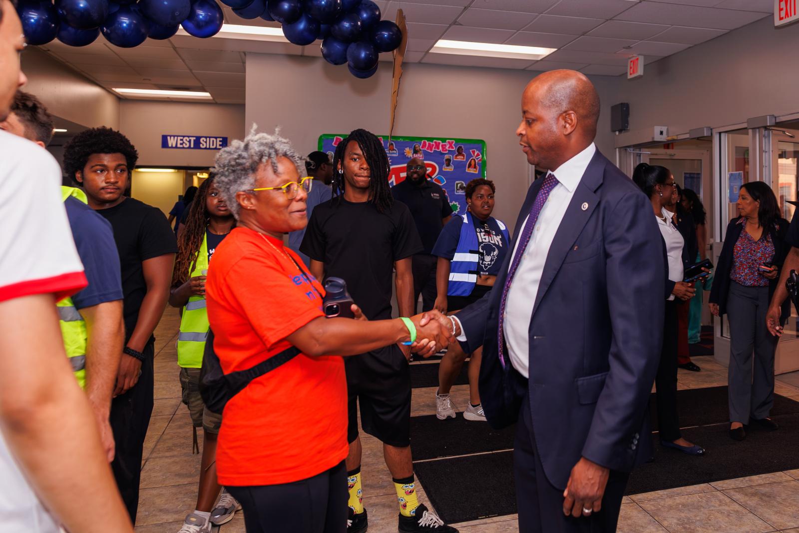 Howard University President Wayne Frederick on the right shaking a woman's hand on the left. There are people in the background walking around