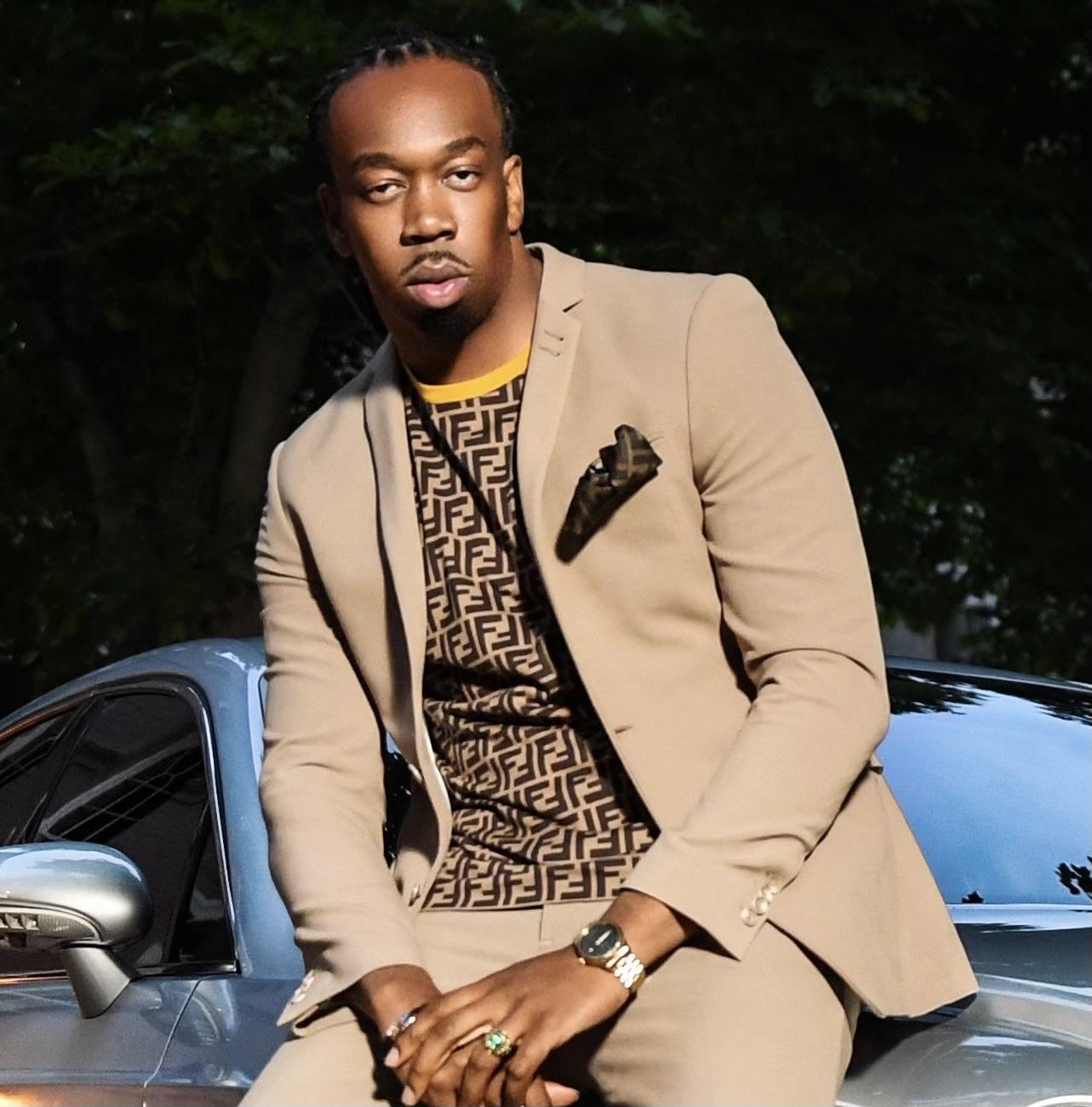 Iran "Bang" Paylor of Models Inc. posing wearing a tan suit and a designer shirt