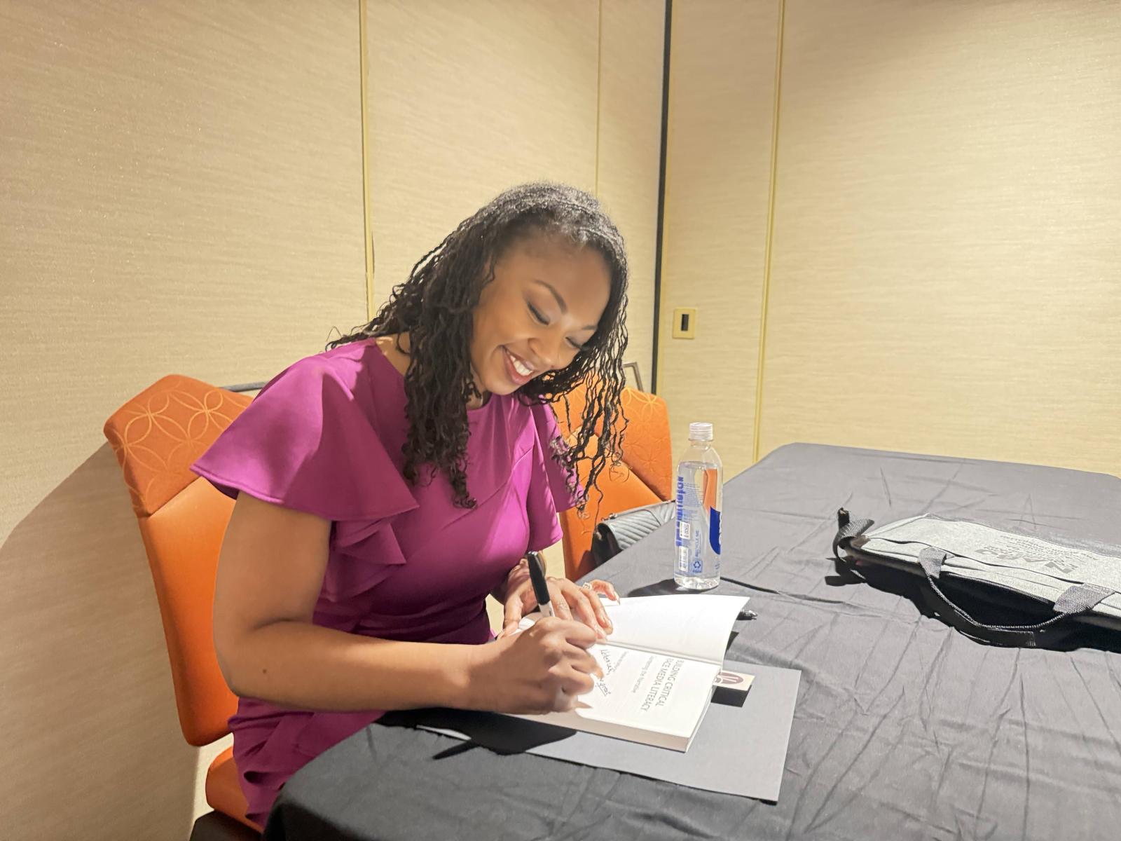 Howard associate professor Christine McWhorter wearing a purple suit signing copies of her book at NABJ Authors Showcase & Bookstore in Atlanta in 2026