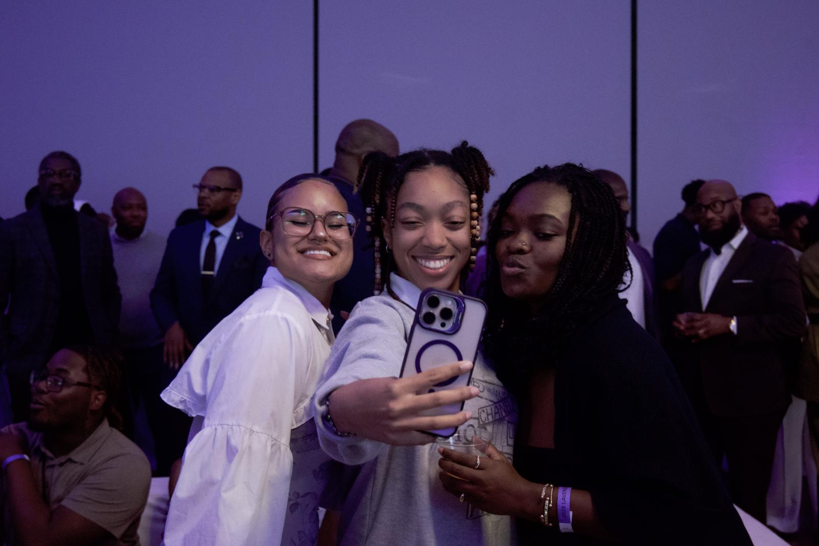 Three students stand side by side talking a selfie at the Lavender Reception 2025